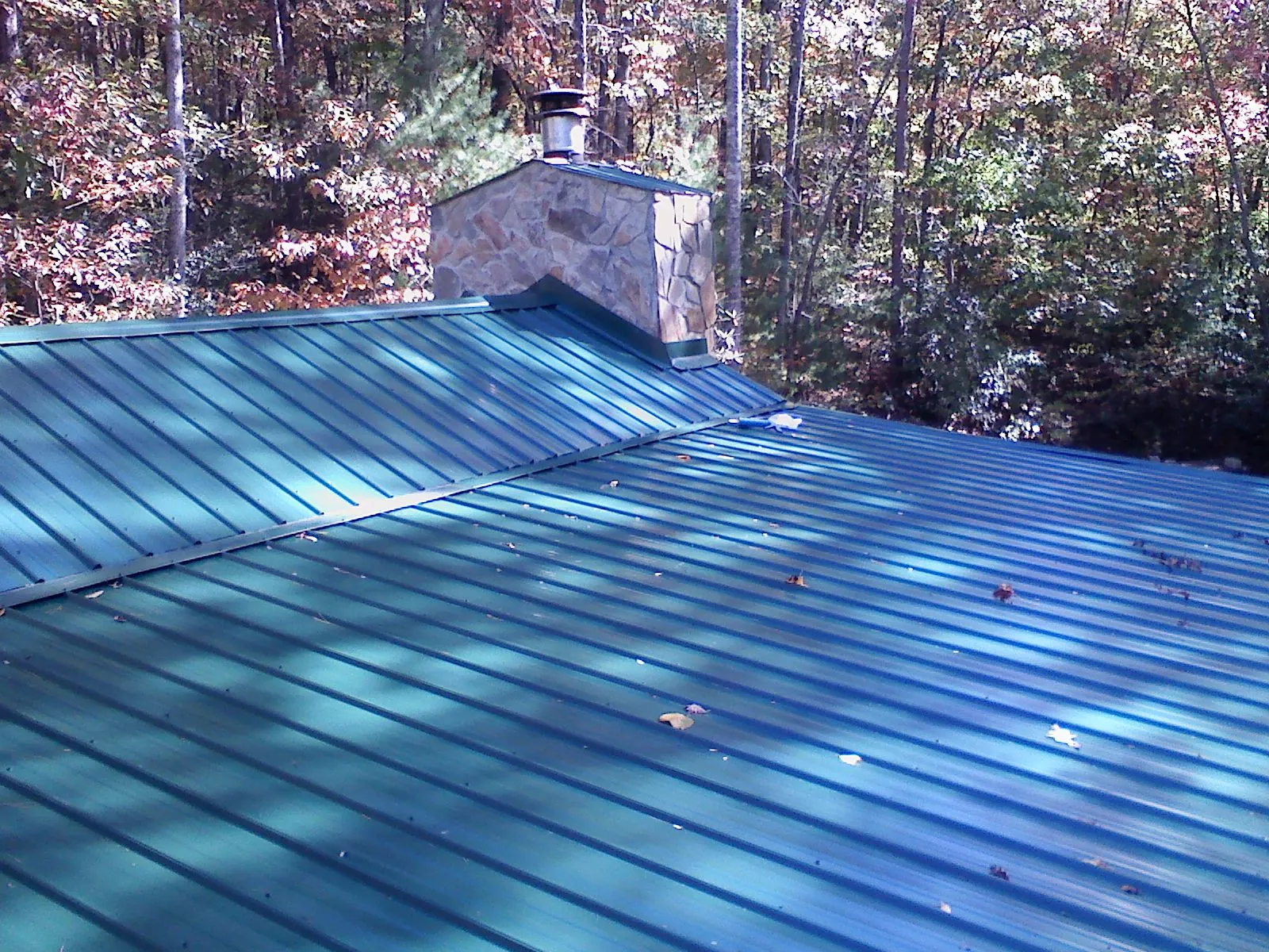 New green metal roof and stone chimney surrounded by autumn woods in Webster